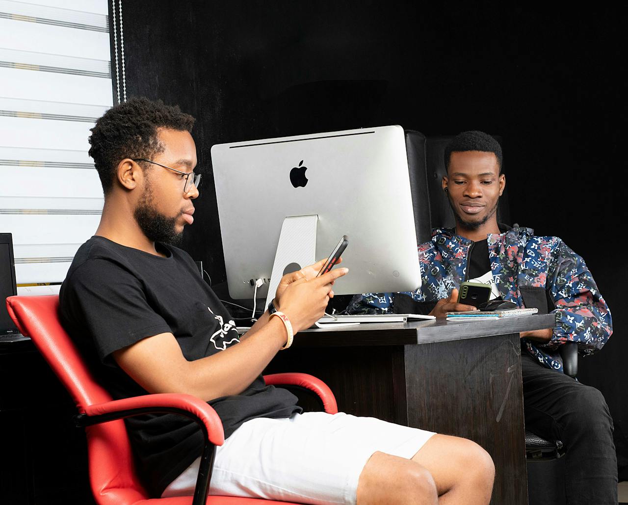 digital Two young men engaged with smartphones at a modern office desk in Port Harcourt.